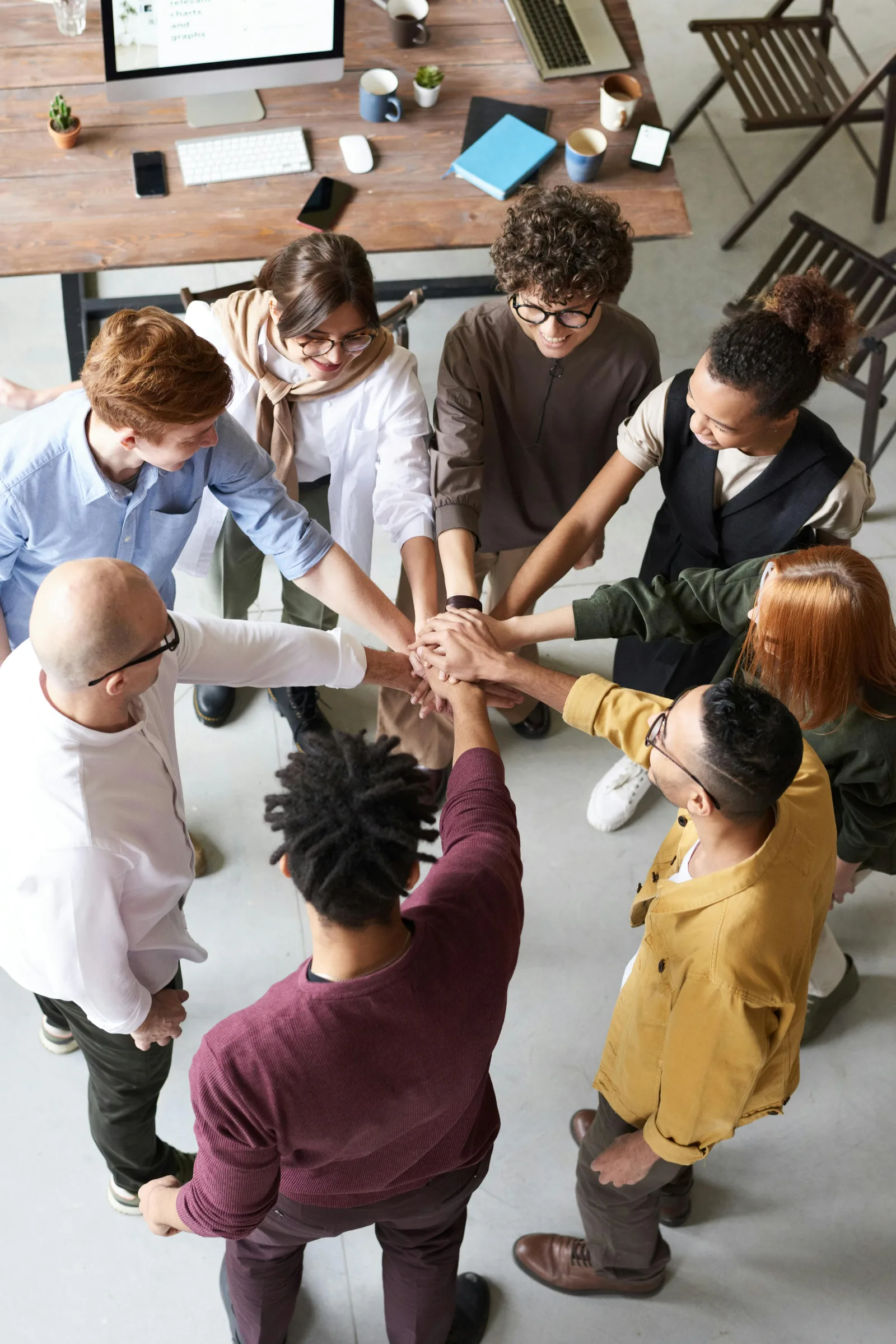 A team in an office standing in a circle with their hands joined in the middle, seen from above