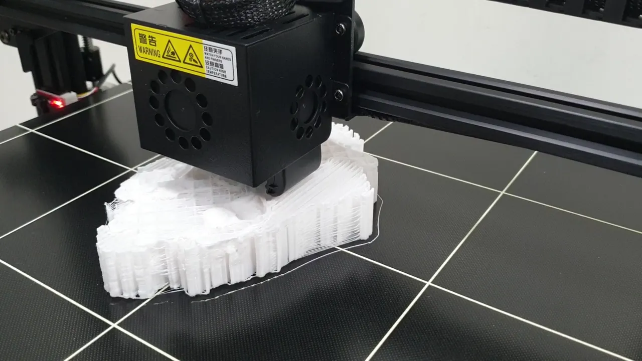 A desktop 3D printer part-way through a job, its nozzle laying down white
                  filament over the flat printed base of a pelvic bone model.