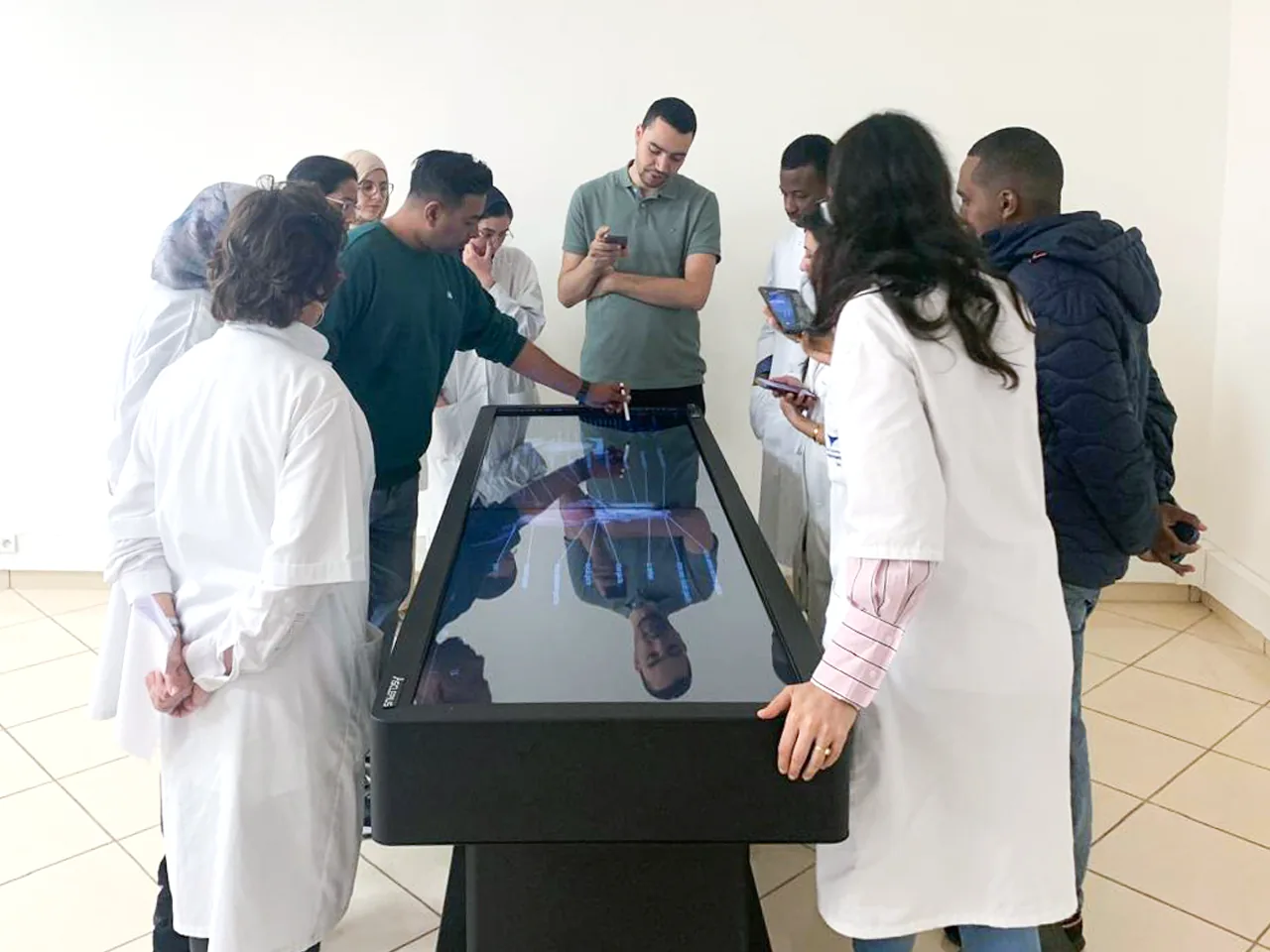 Students and clinicians in white coats gathered around an Asclepius virtual dissection table, one of them drawing on the screen with a stylus while the others look on