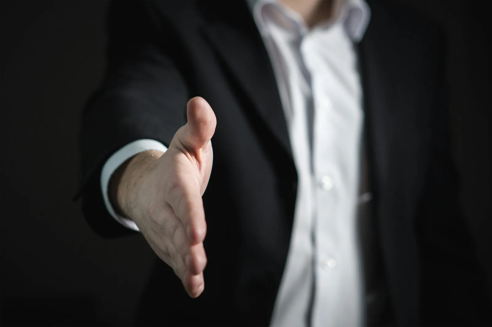 A person in a dark suit reaching forward to offer a handshake