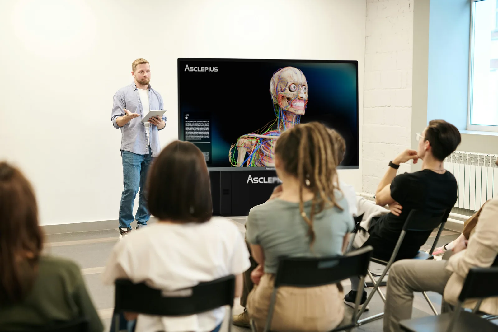A small group seated around a TBK-65 4K table displaying a full-body
                    anatomical model, with an instructor leading the session.