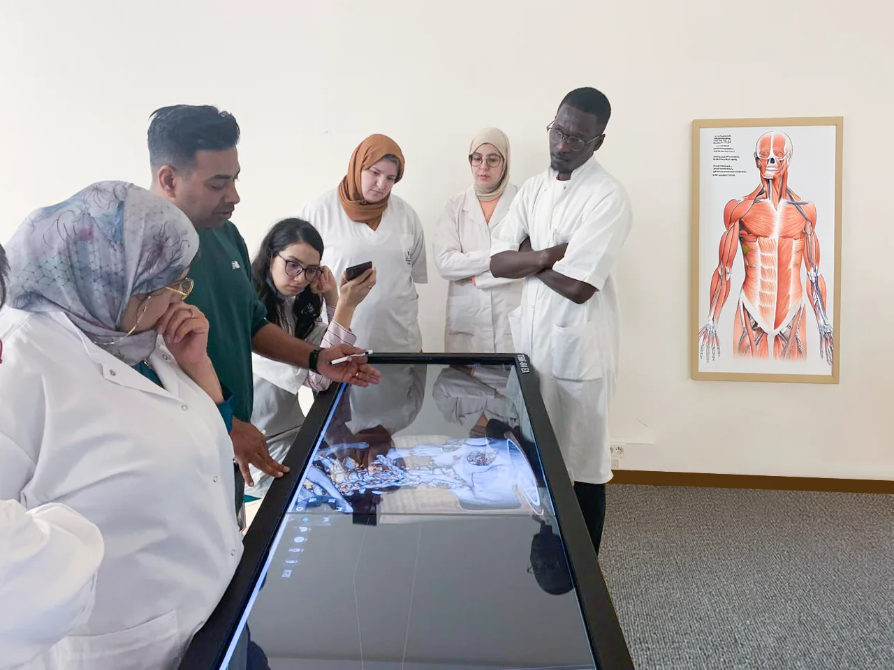 Clinicians and students gathered around an Asclepius dissection table, one of them using the stylus on the touchscreen