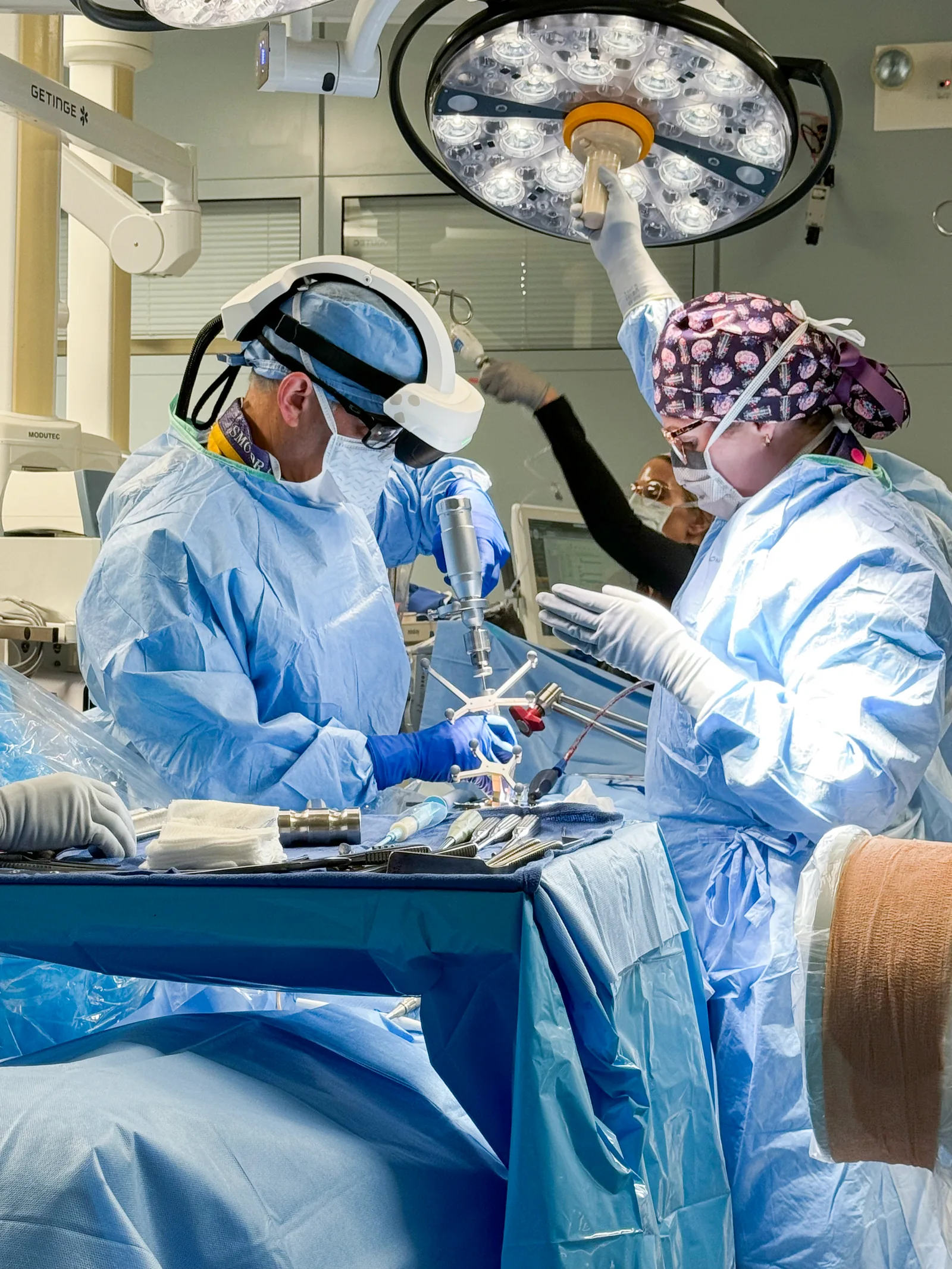 A spine surgeon wearing the Caduceus S AR headset at the operating table, working with a navigated instrument and reference array